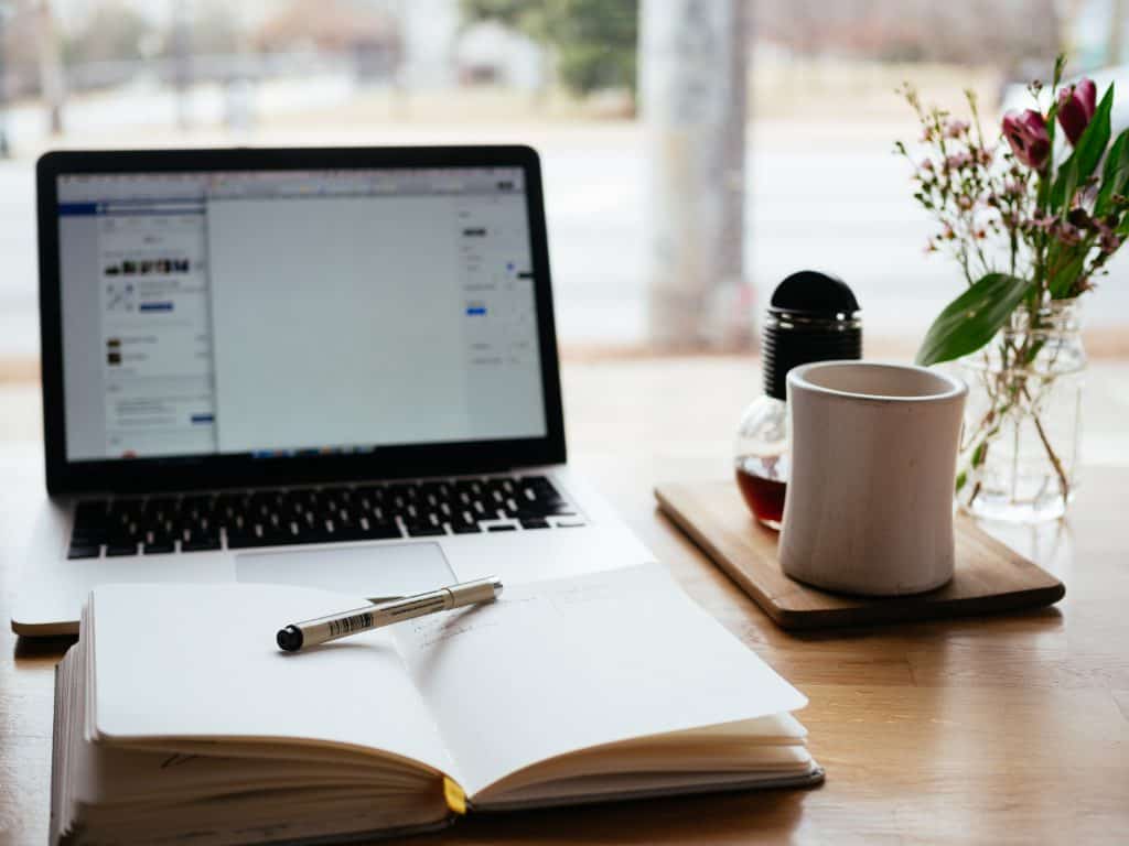 notebook with pencil open in front of laptop with facebook and blank word processing document coffee mug nearby