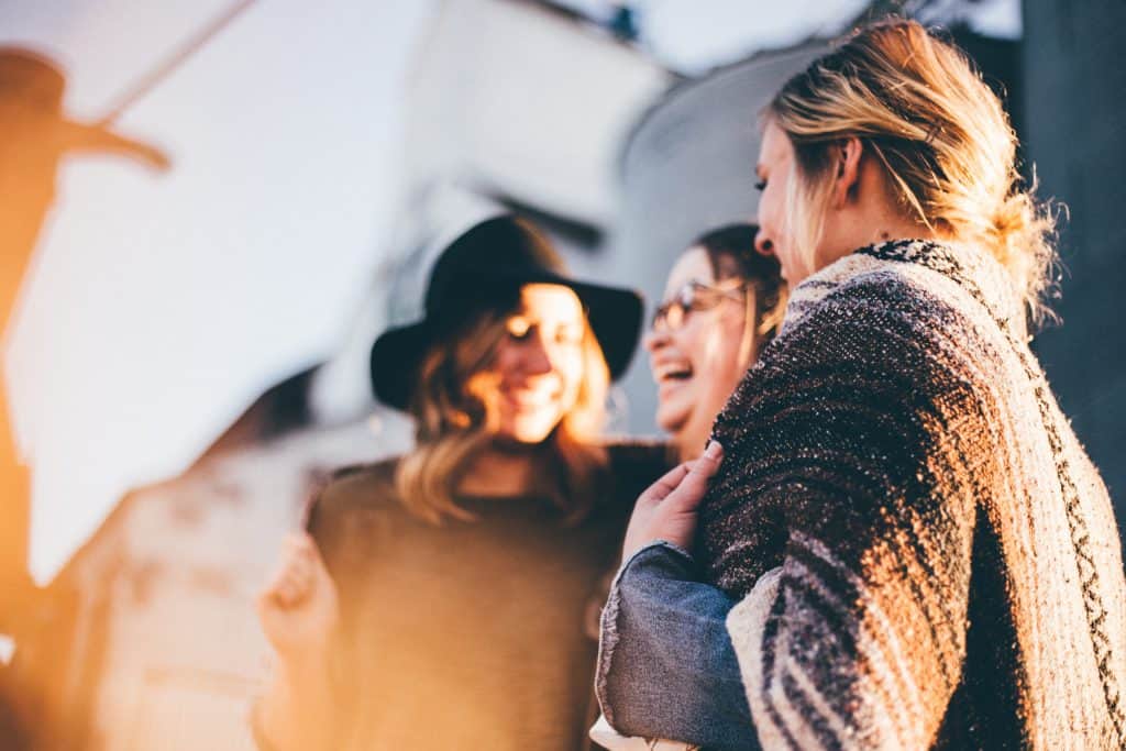 group of women talking laughing in warm fall outfits wearing felt hat woven blanket