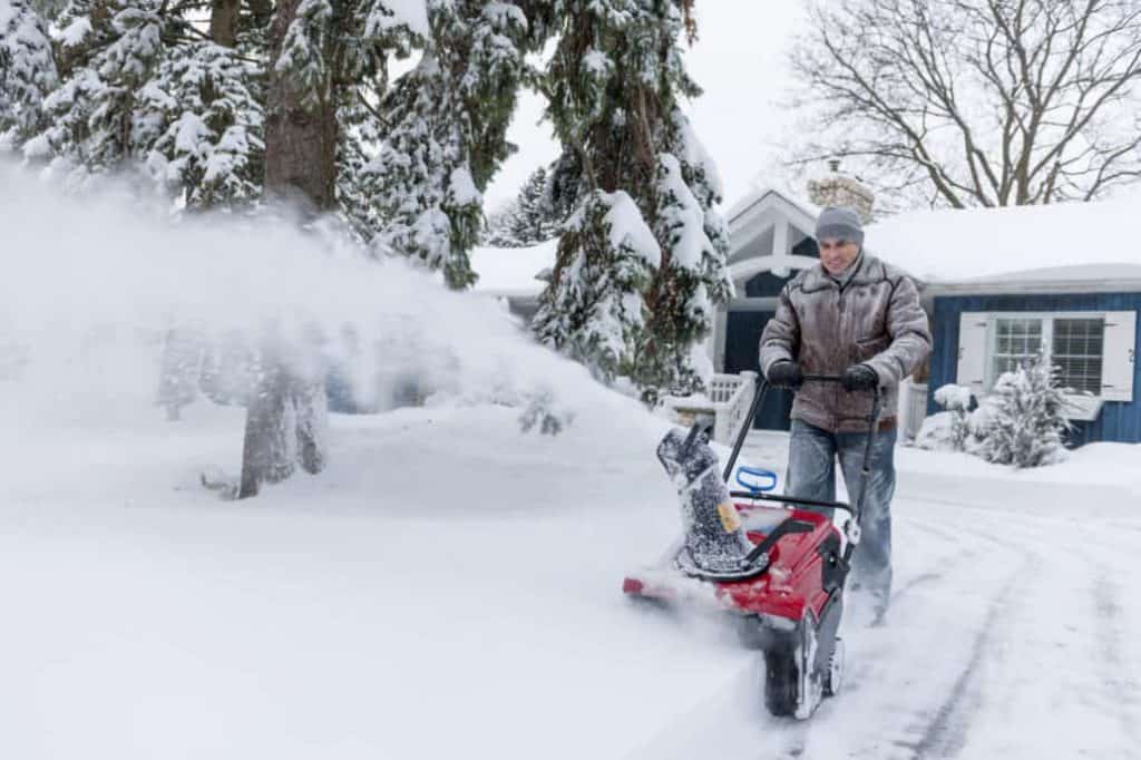 man running snowblower in front of blue house