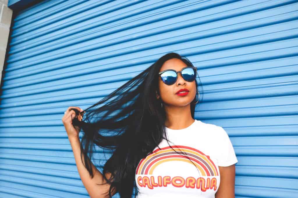 tan woman with black hair wearing sunglasses and california shirt posing in front of blue storage unit door