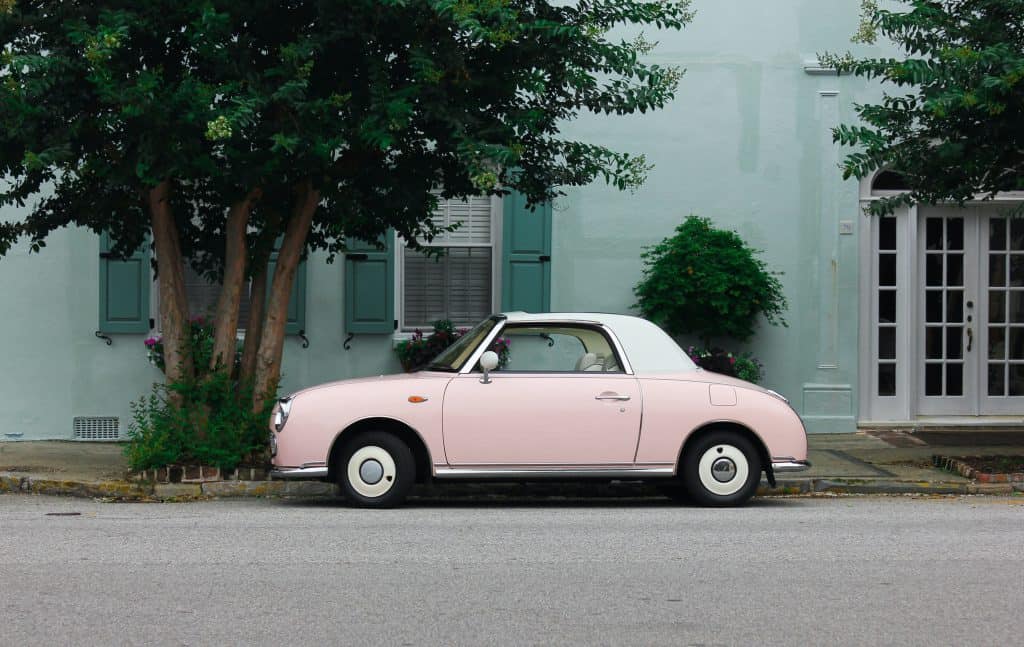 pink 2 door vintage car parked outside under tree