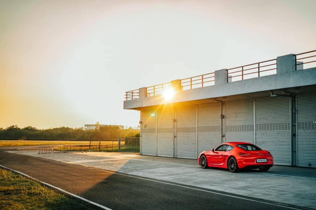 red sports car parked in front of warehouse doors next to road at sunset