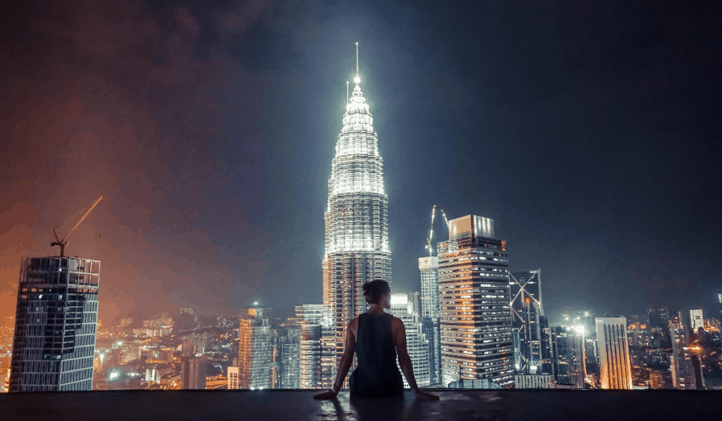 kuala lampur malaysia mujer mirando un gran rascacielos de la ciudad iluminado por la noche