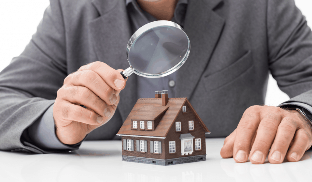 man in suit holding magnifying glass over toy house home inspection