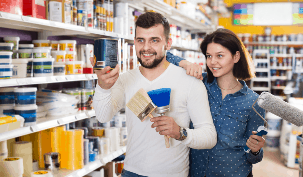 hombre mujer pareja en tienda de pintura sosteniendo brochas rodillo de pintura eligiendo colores de pintura